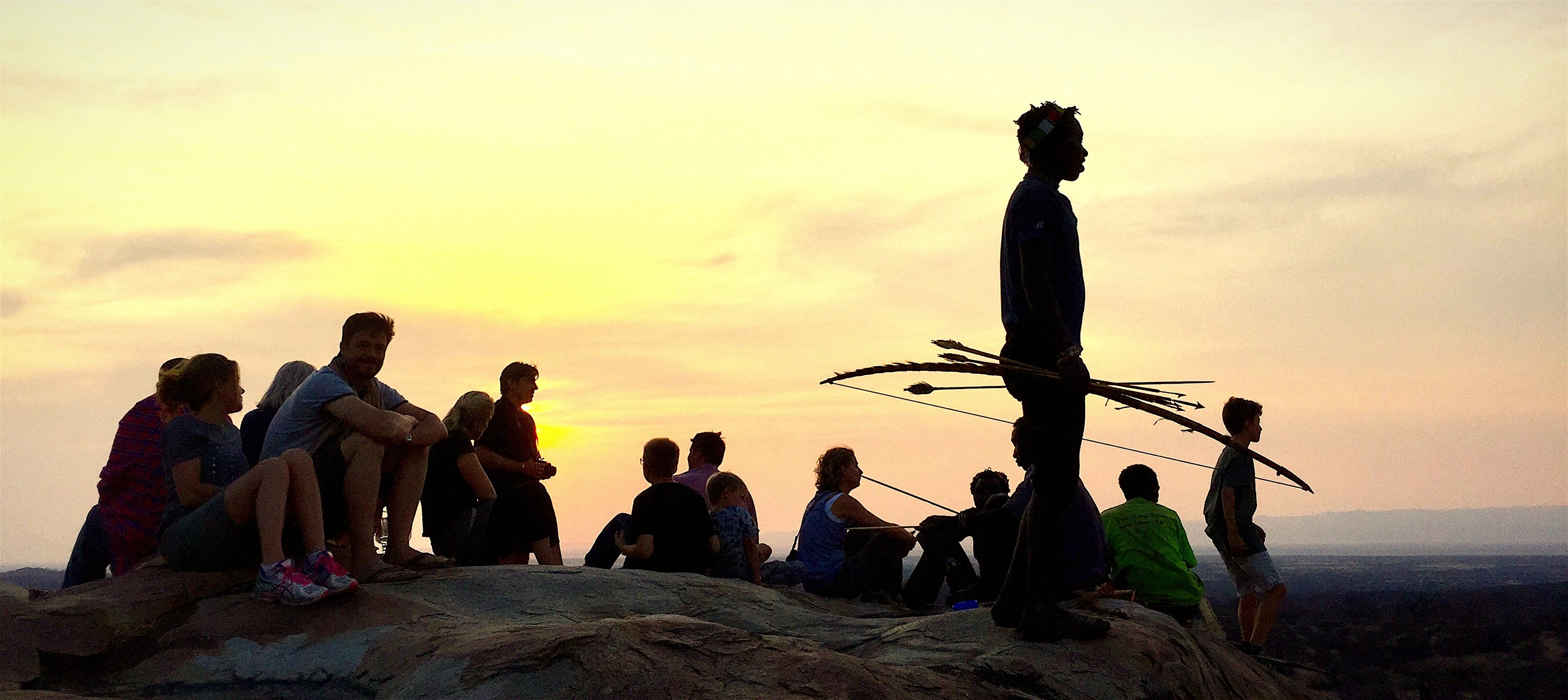 Guests seated with Hadza guides as the sun sets over the plains