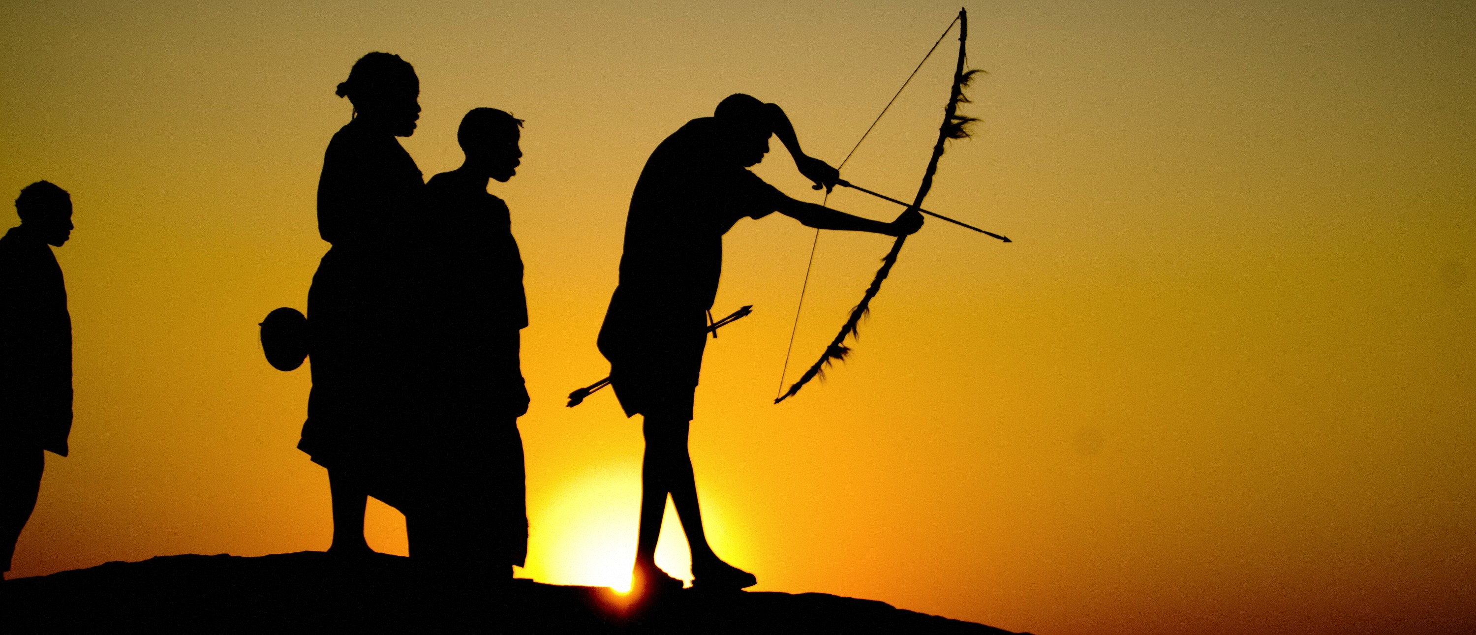 A Hadza hunter drawing his bow at sunset in the Yaeda Valley