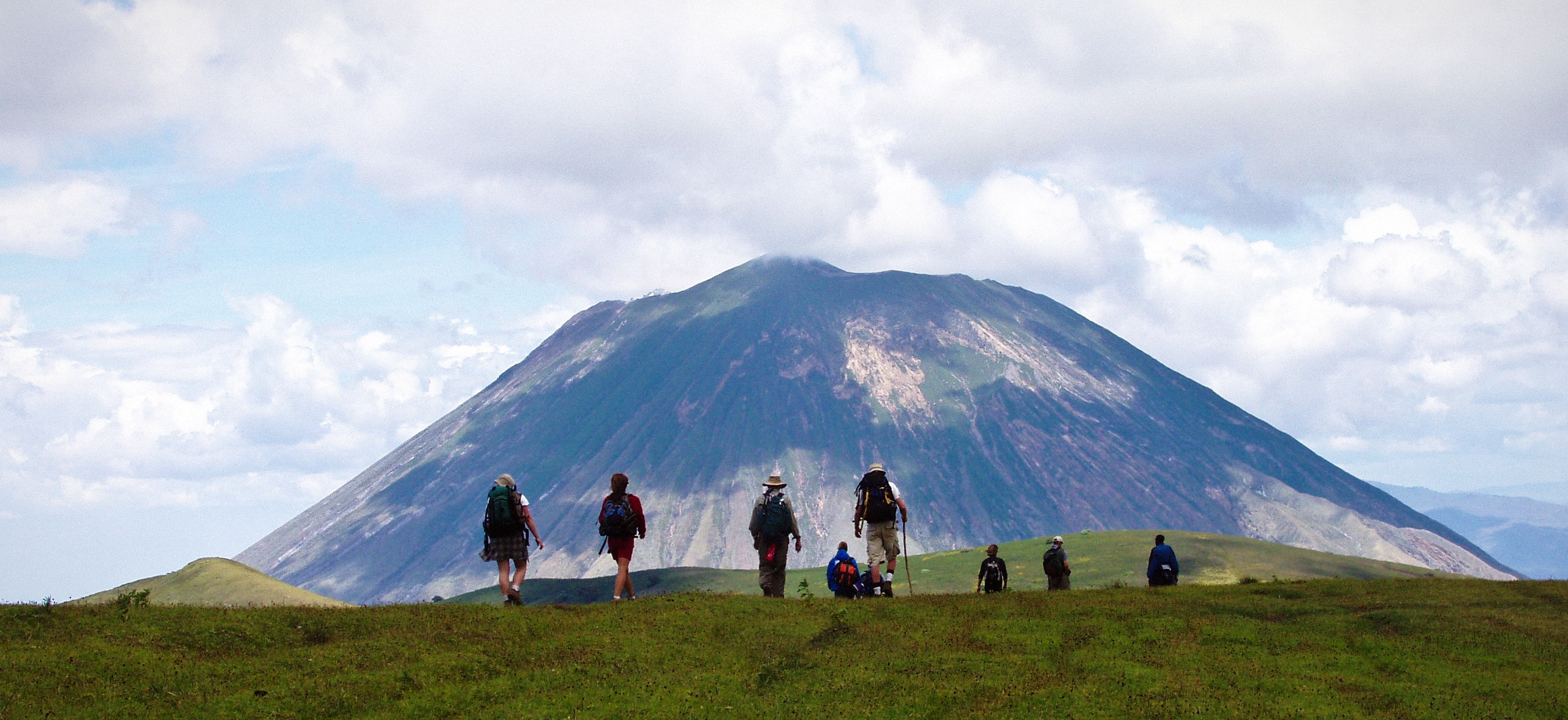 Hikers crossing green slopes beneath Oldonyo Lengai volcano
